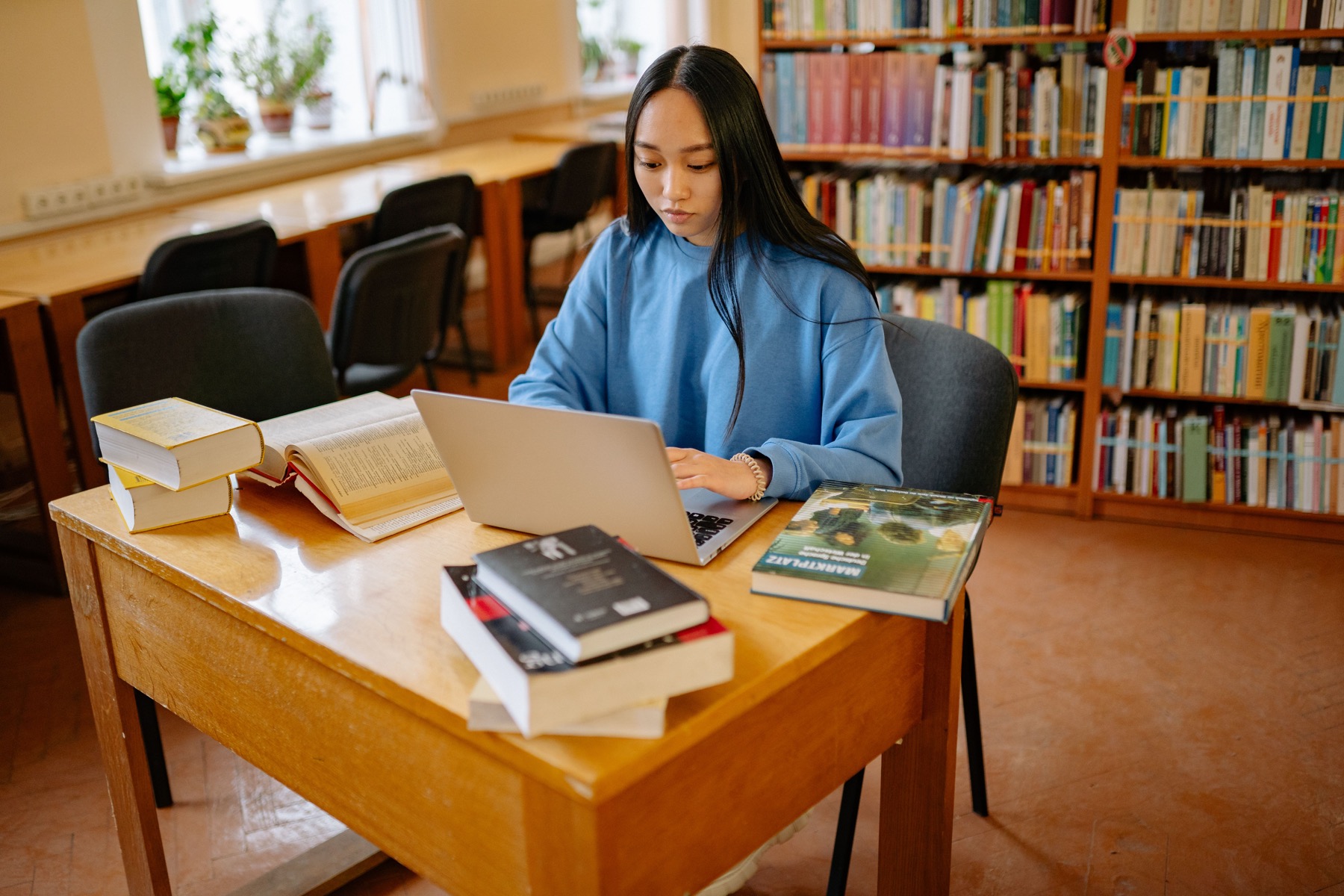 Focused high school student reflecting on her experiences while working on a laptop in a library.
